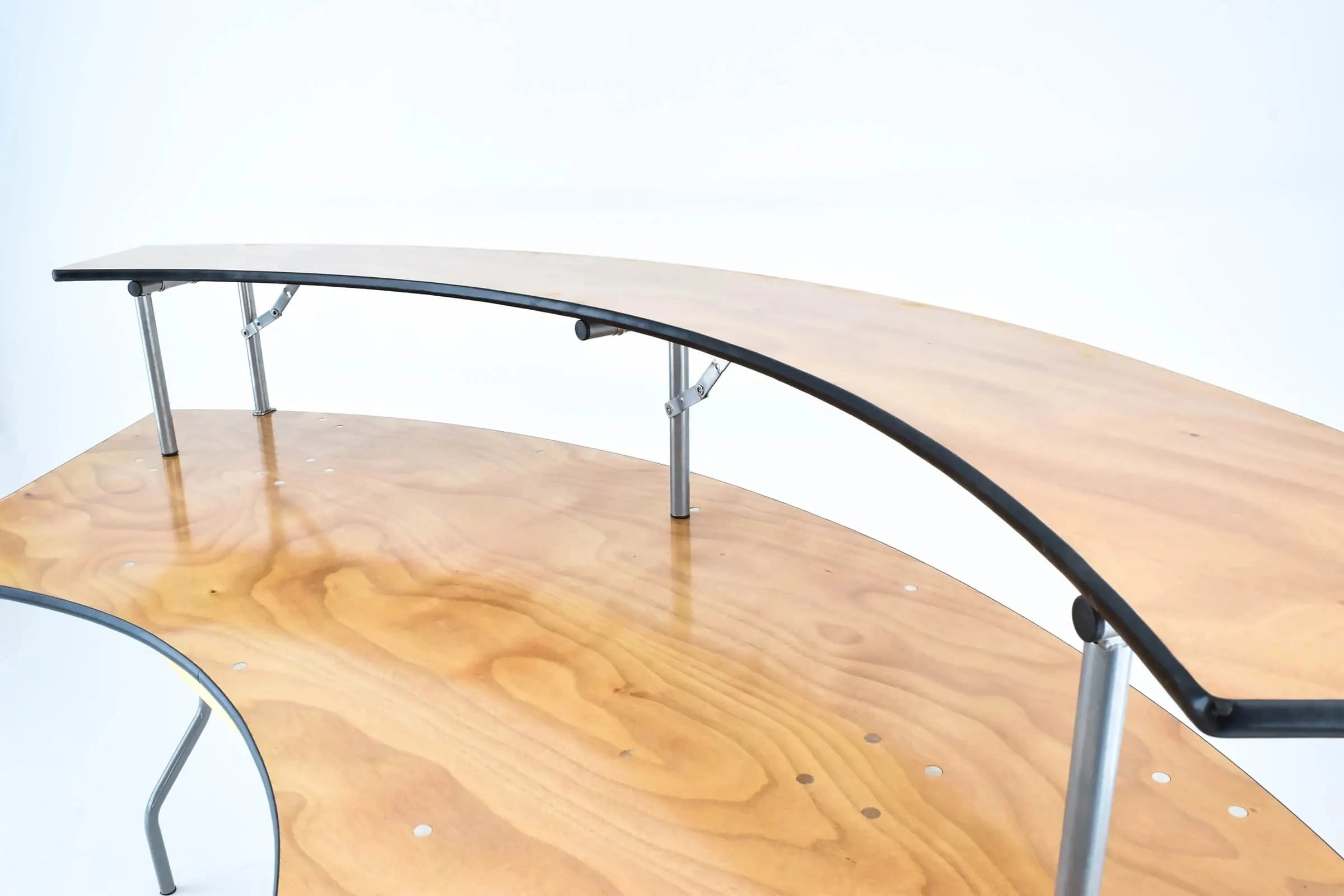 Close view of both tiers on the extended serpentine bar table showing the raised shelf and main table surface relationship.
