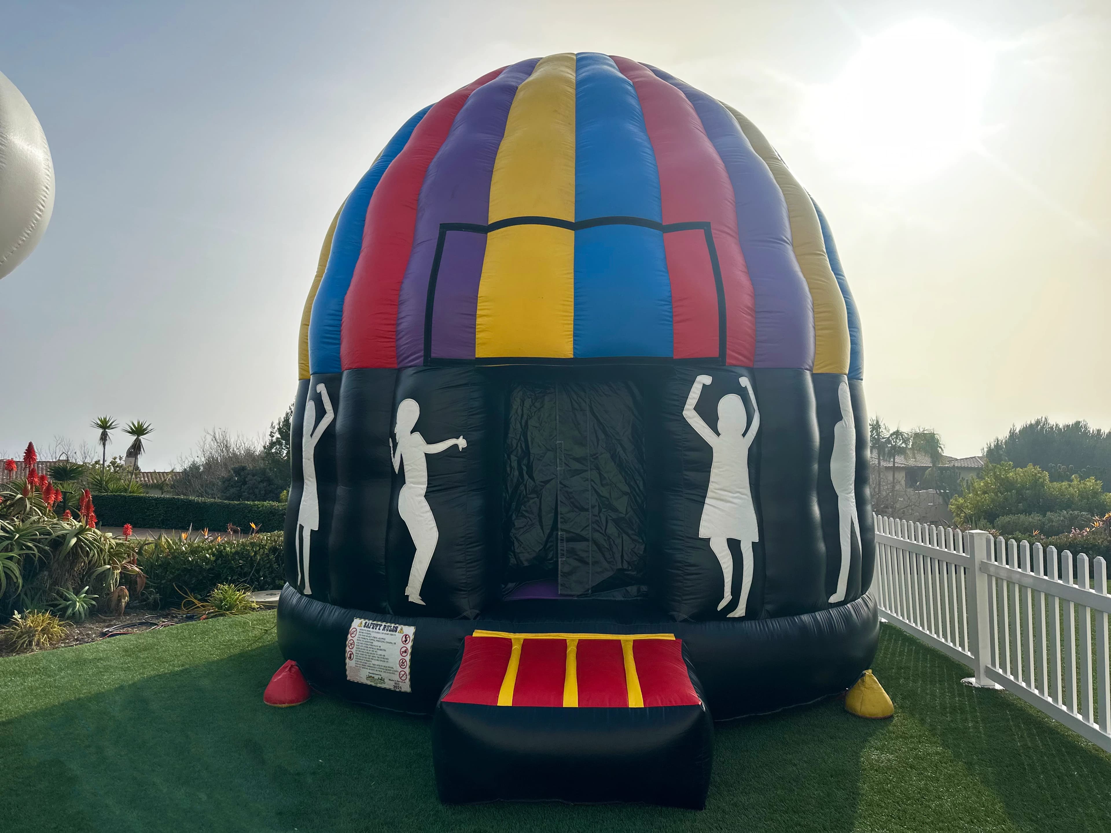Outdoor side angle of the Incredible Dance Party Dome Jumper showing its circular shape and colorful design.