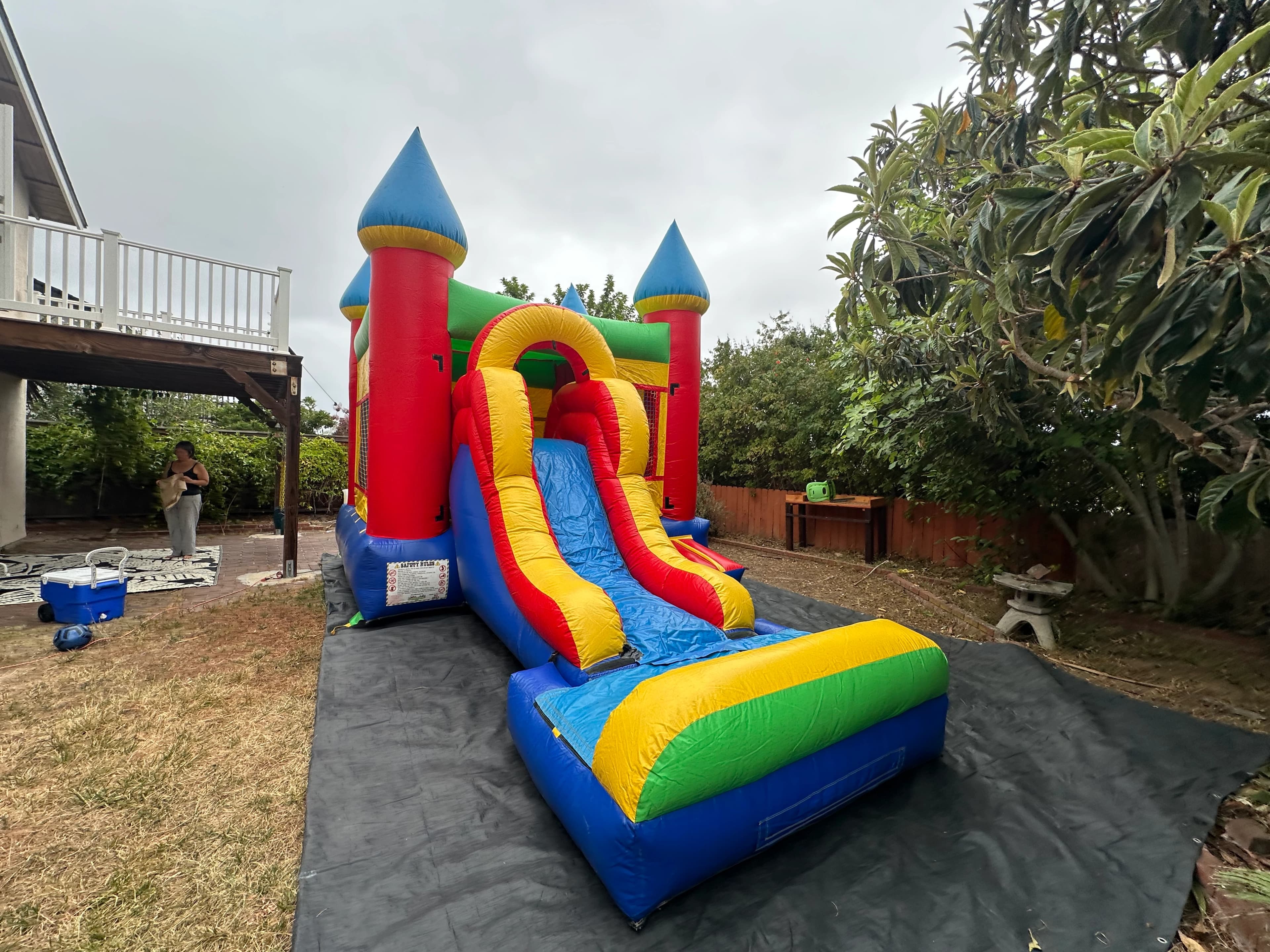 Side view of the Rainbow Castle Combo showing the slide, bounce area, and colorful turrets on grass.
