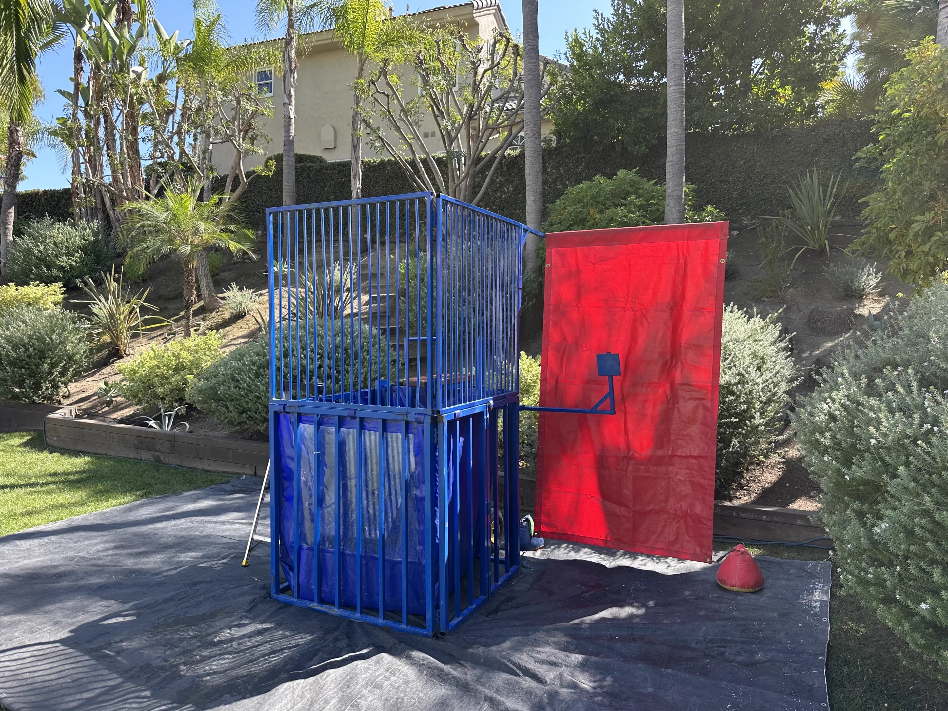 Wide outdoor setup of the Standard Blue Dunk Tank positioned on grass with target cage and access ladder clearly shown.